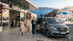 A professional chauffeur greeting a couple for premium Santorini airport transfers at the JTR arrivals terminal.